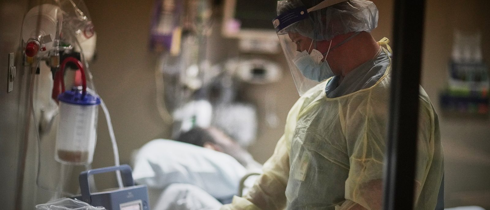 A clinician in a protective gown, mask and face shield checks on a ventilated patient during a night shift in an intensive care unit.
