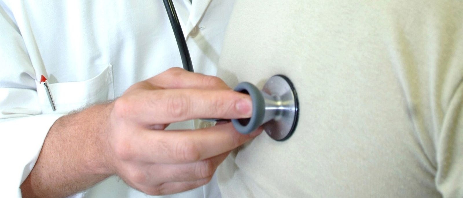 A clinician in a white coat listens to a patient with a stethoscope during a physical examination.