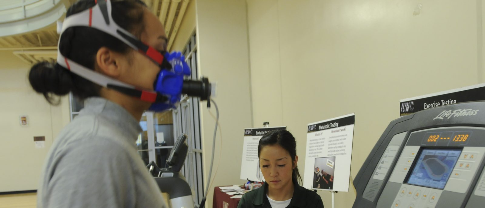 An athlete wearing a gas-analysis face mask runs on a treadmill during a metabolic exercise test while a clinician monitors the results.